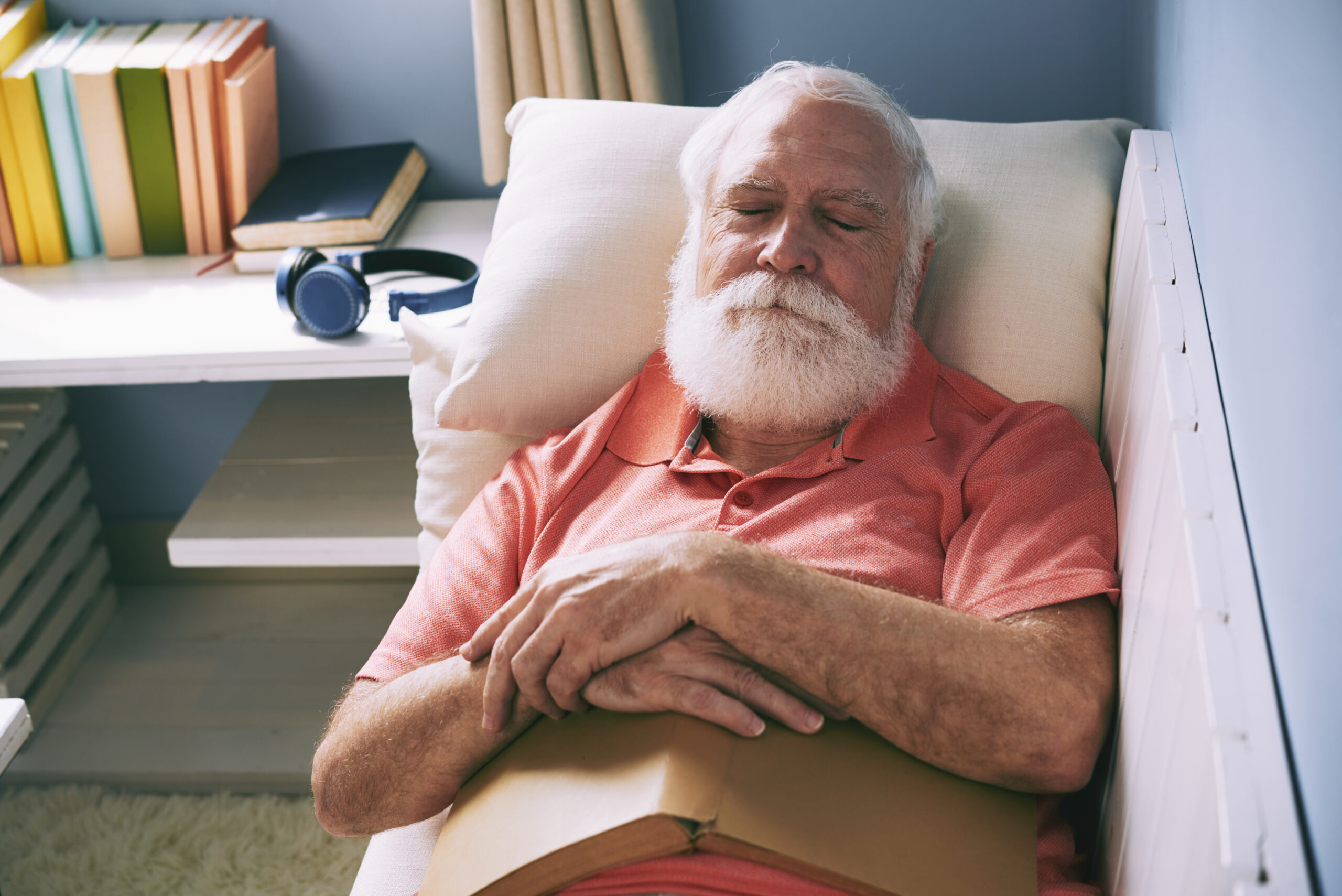 Senior man with white beard napping on sofa with book on his belly